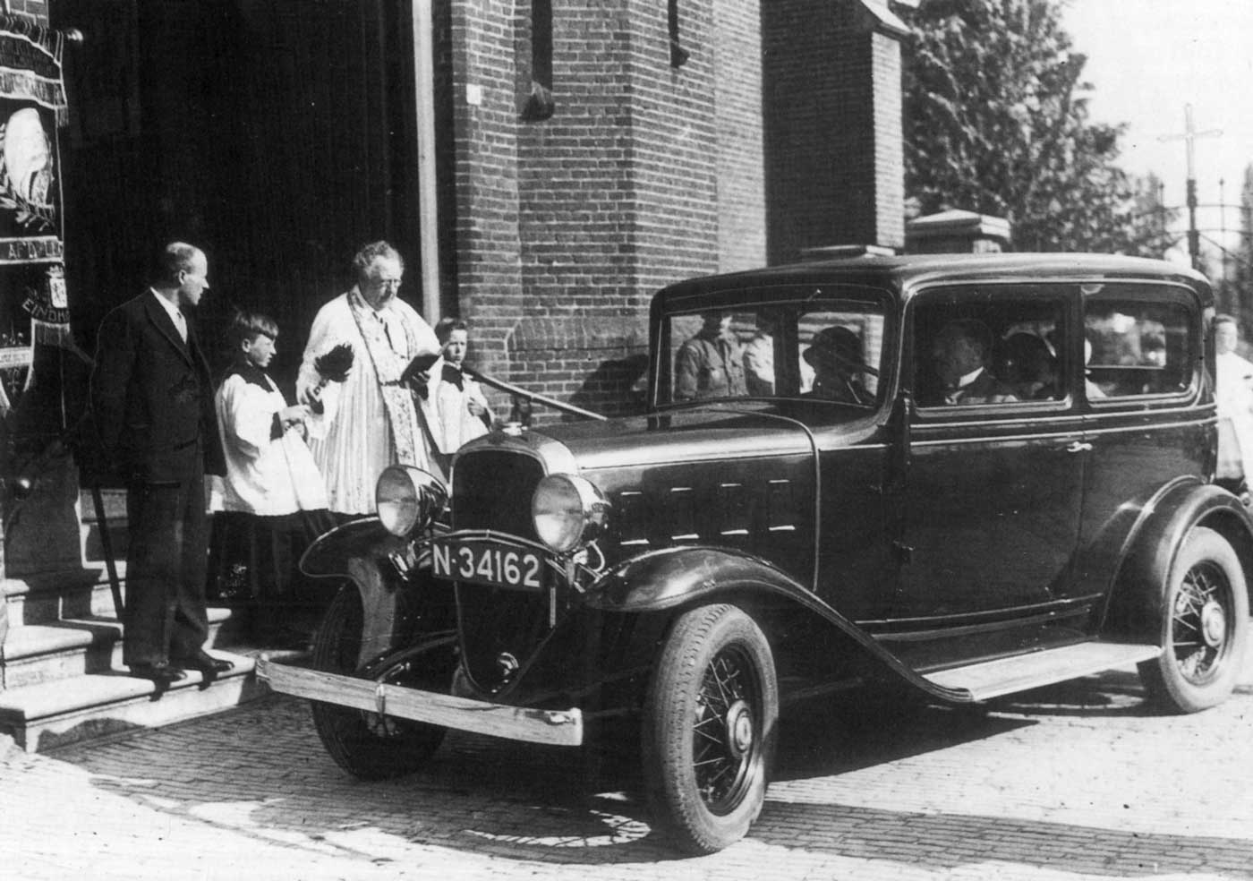 Pastoor Werners zegent in 1933 de auto met kenteken N-34162 (bron: Ach Lieve Tijd. 3. De boeiende historie van Eindhoven, de Eindhovenaren en hun geloof, blz. 55)